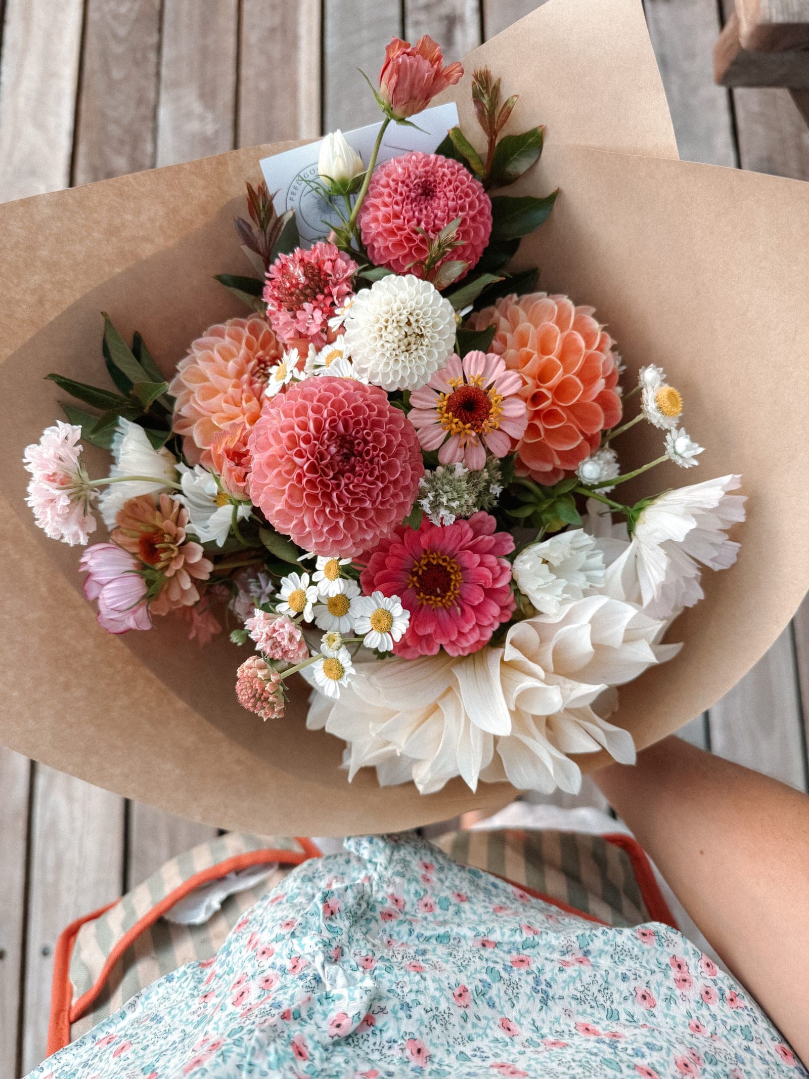 A large bouquet in kraft paper — pompom dahlias, zinnias and daisies in coral, peach and cream.