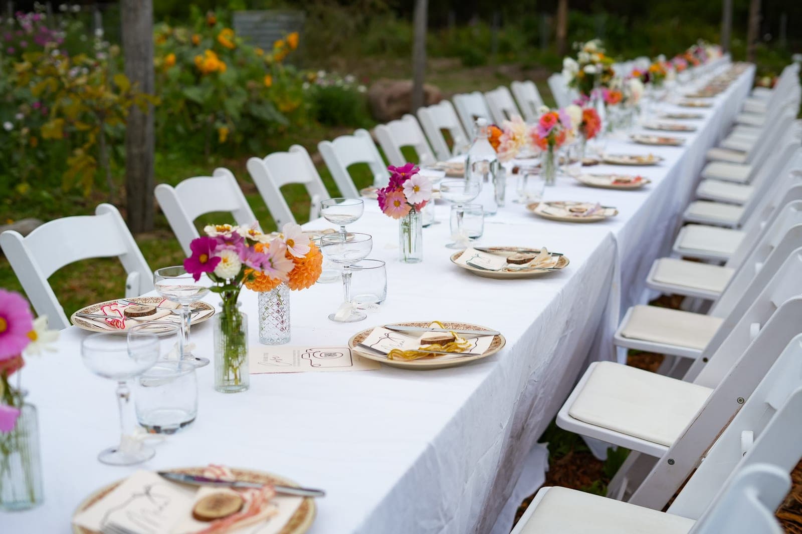 A long white table set for a wedding in the rows, posies down its length.