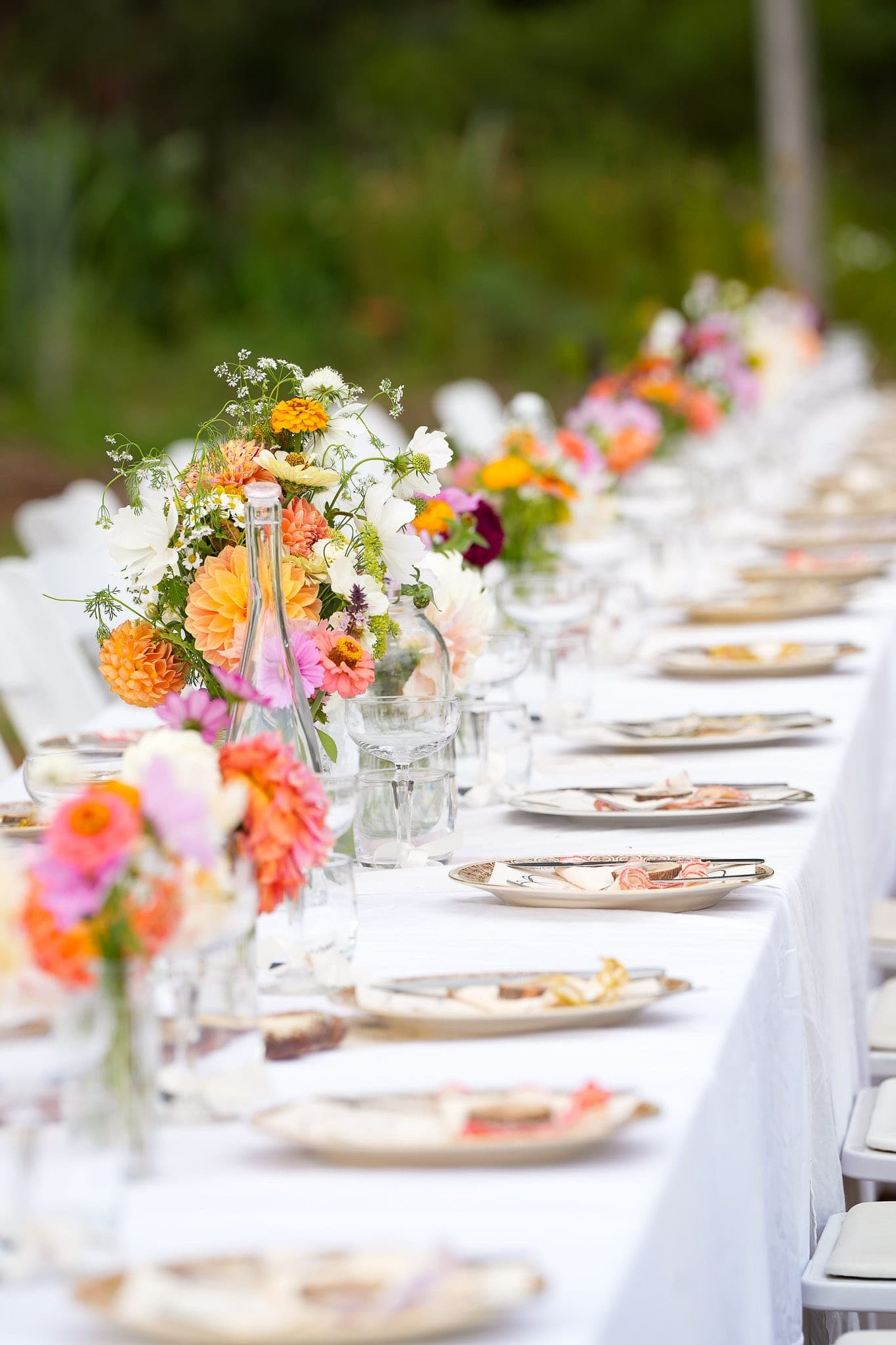 Small posies of zinnias, dahlias and cosmos running down a set wedding table.