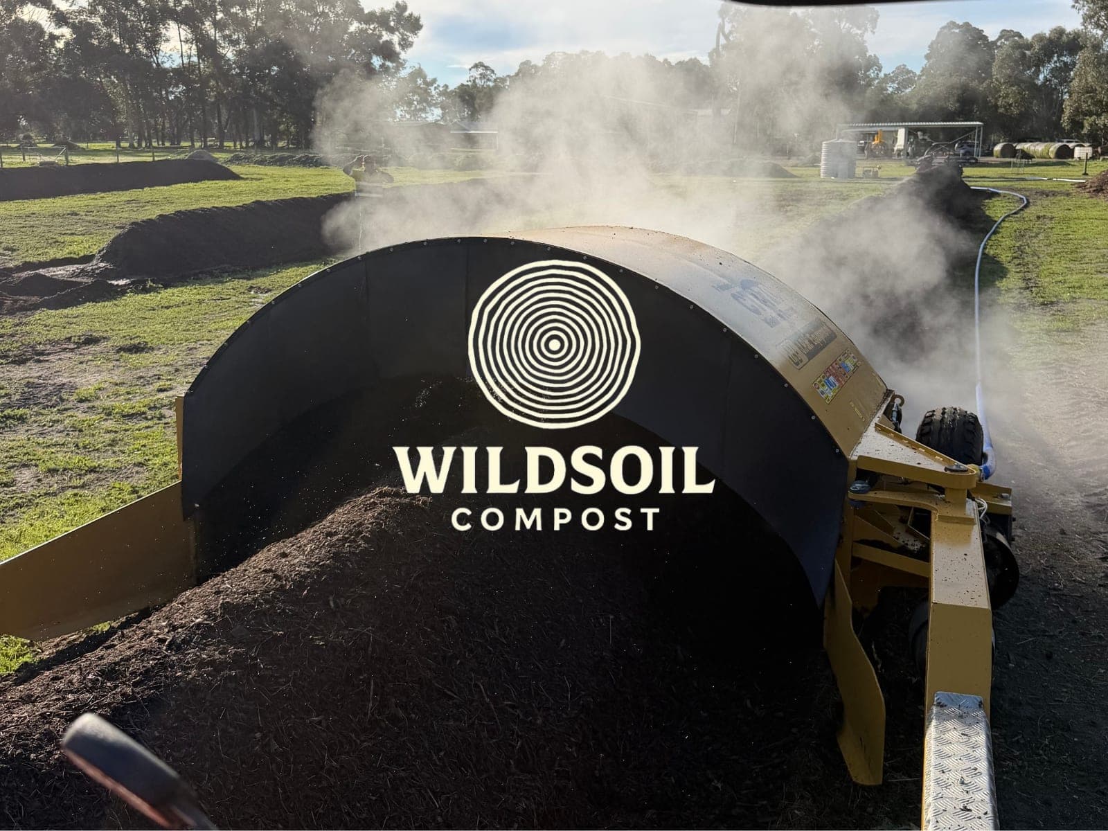 The Wildsoil Compost turner working a steaming windrow, branded with the logo.